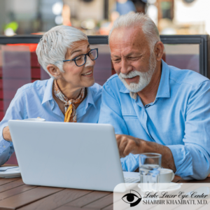 older couple with grey hair looking at laptop screen while dining outside