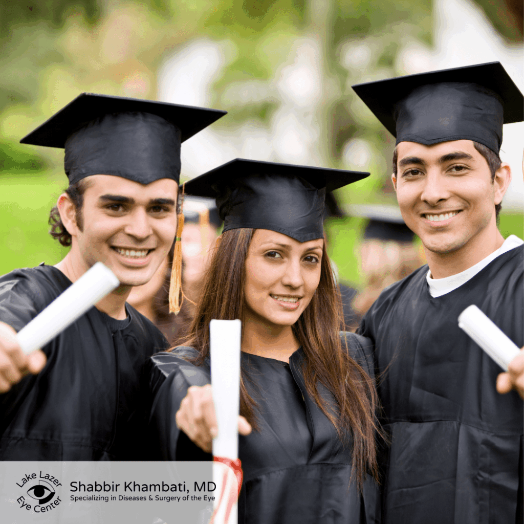 Three smiling graduates in caps and gowns holding diplomas at an outdoor commencement ceremony.
