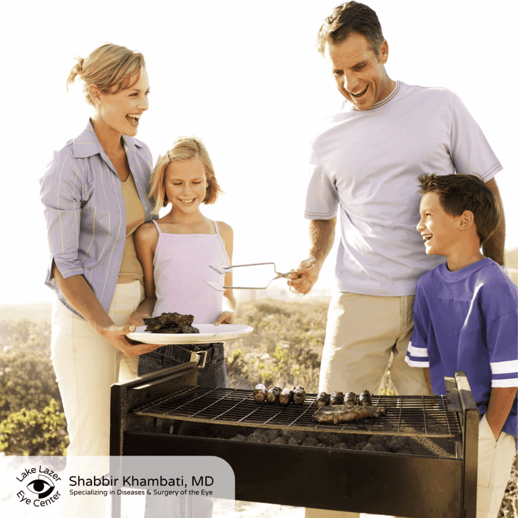 Family of four smiling while grilling outdoors together at a barbecue.